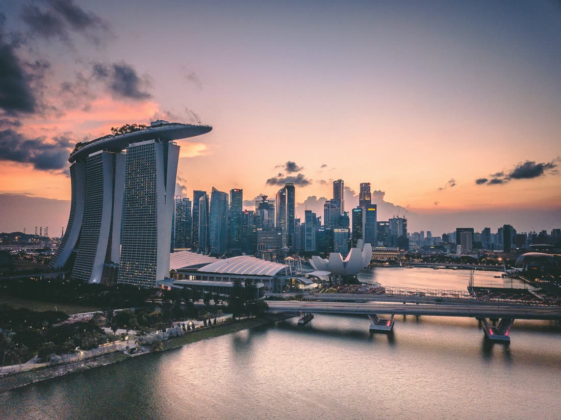 Marina Bay in Singapore at sunset, with the waterfront hotel and the lotus-shaped museum lit against a peach-coloured sky