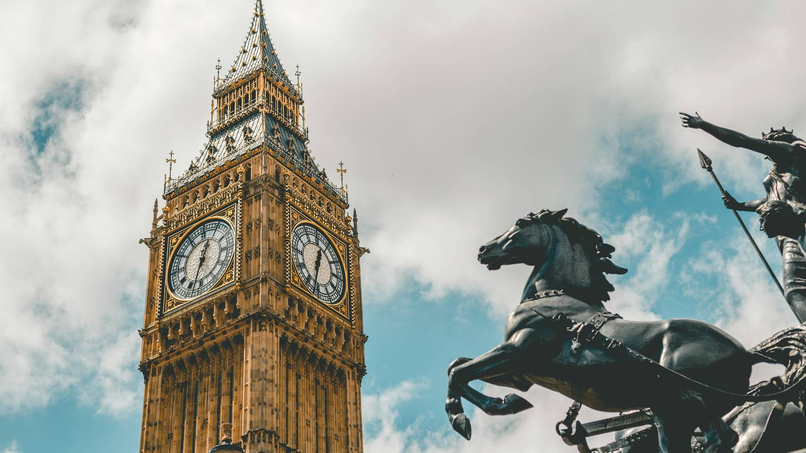The clock tower and the bronze statue of a warrior in a chariot in London, seen from below against a cloudy sky